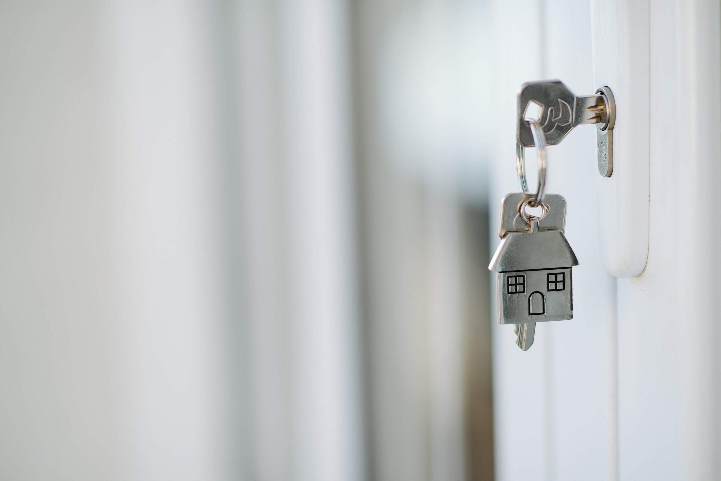 Een huissleutel met een zilveren huisje als sleutelhanger in het slot van een witte voordeur.