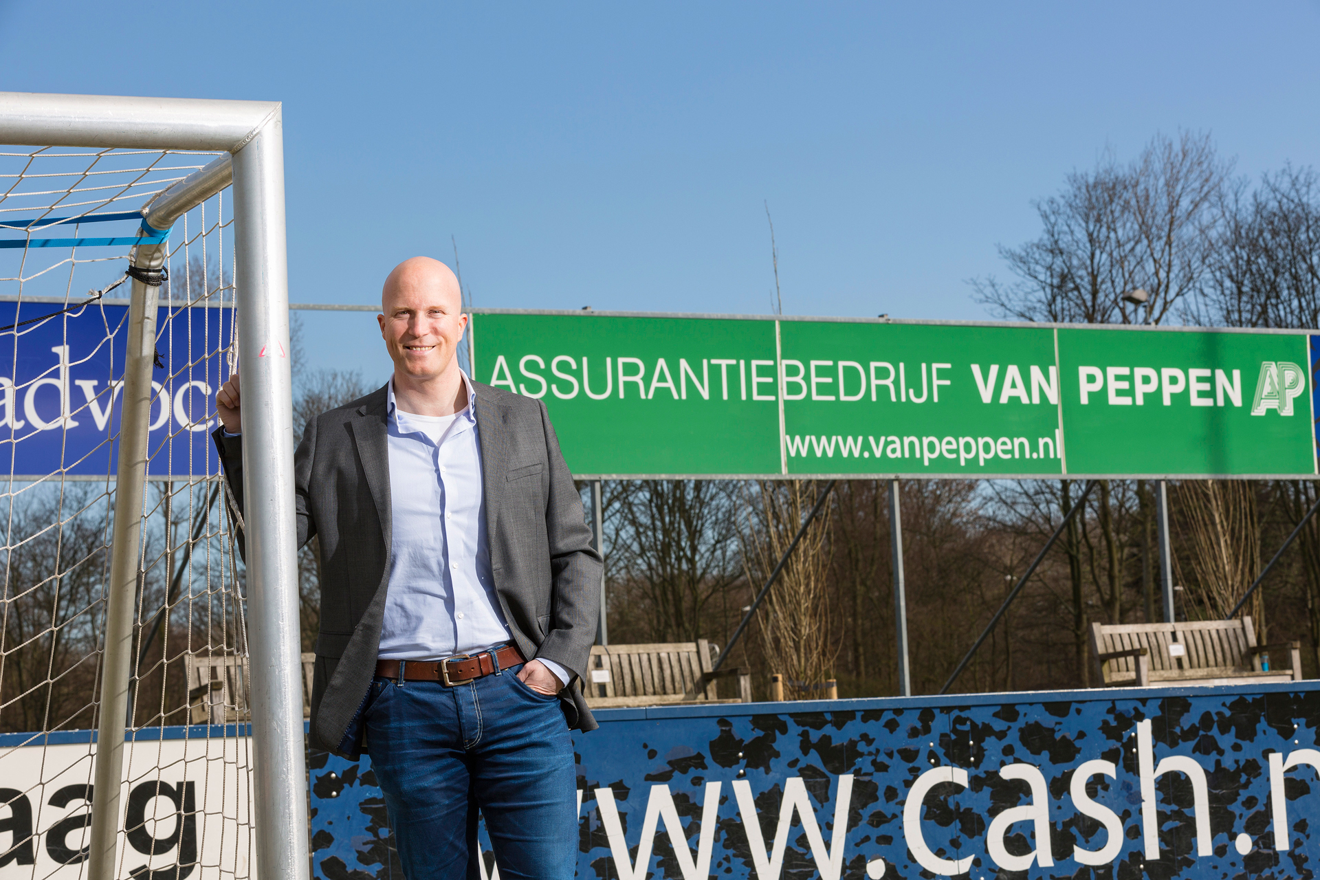 Ivo van Peppen bij een voetbalveld, naast een reclamebord van Assurantiebedrijf Van Peppen.